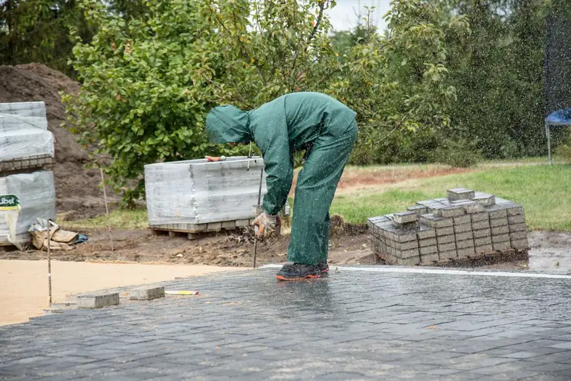 Groundworker laying a block paving edge course on a concrete bed on a damp day in north Manchester